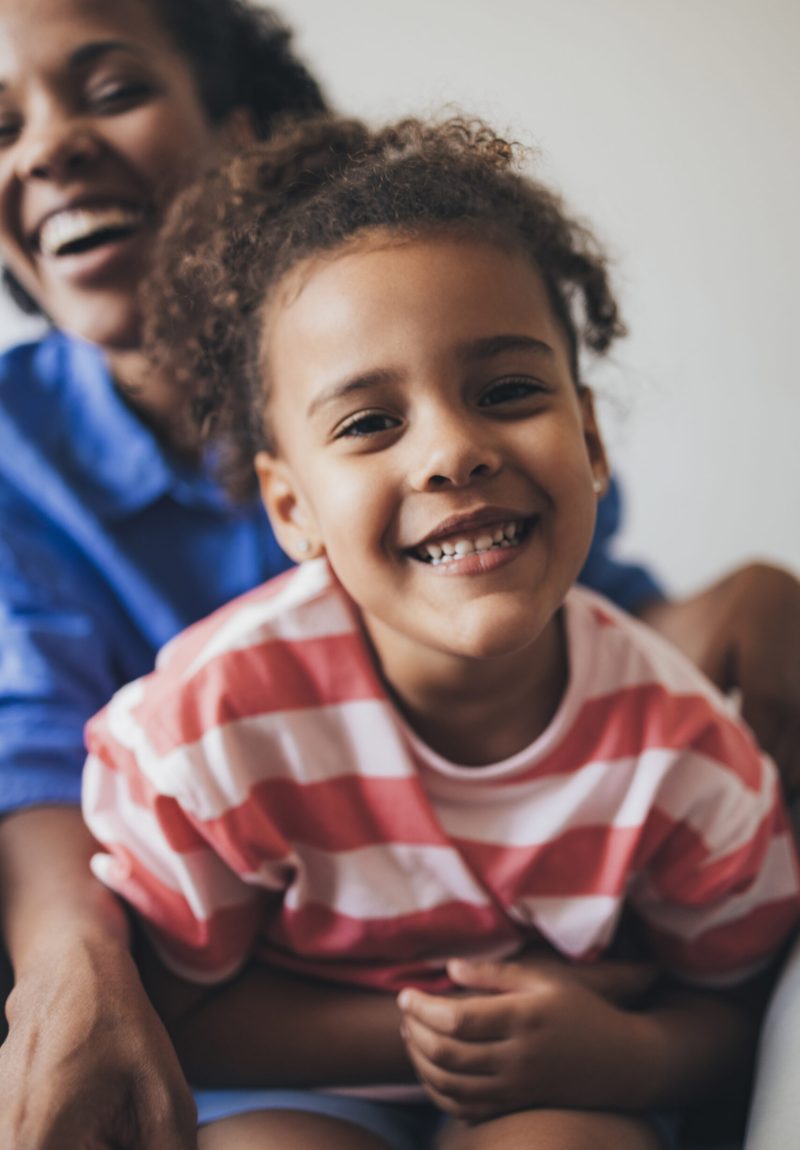 Portrait of a Latin mother and her daughter sitting on the bed, smiling.