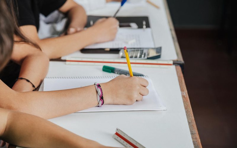 Midsection of schoolchildren writing at desk in classroom