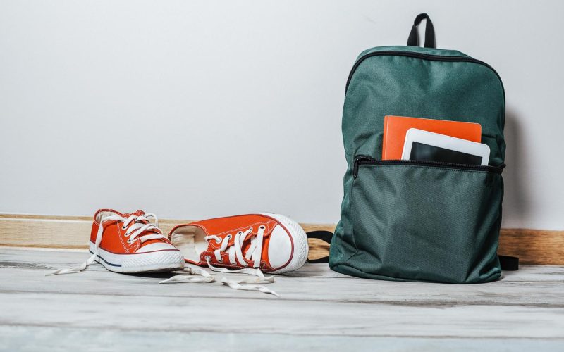 Red sneakers with school bag on wooden background
