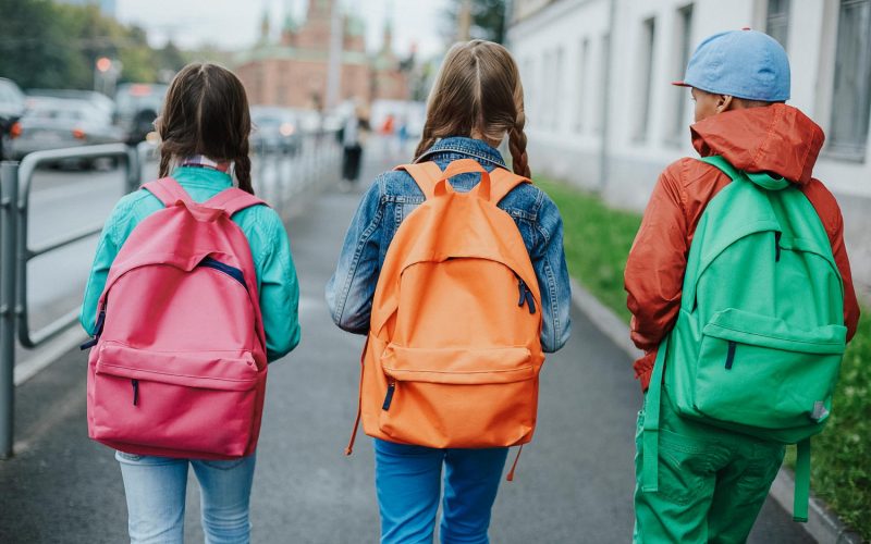 Backs of schoolkids with colorful rucksacks moving in the street