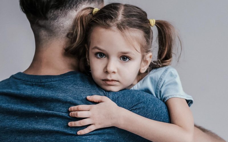 Sad little girl hugging her father on grey background