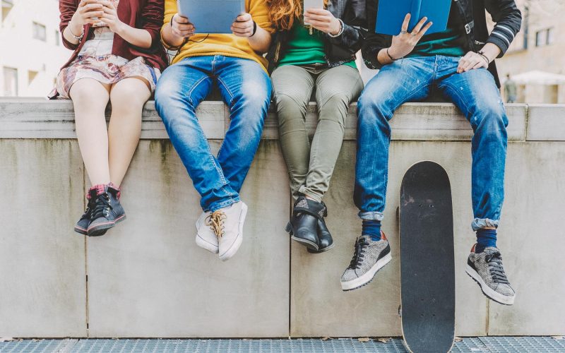 Group of teenagers making different activities sitting in an urban area