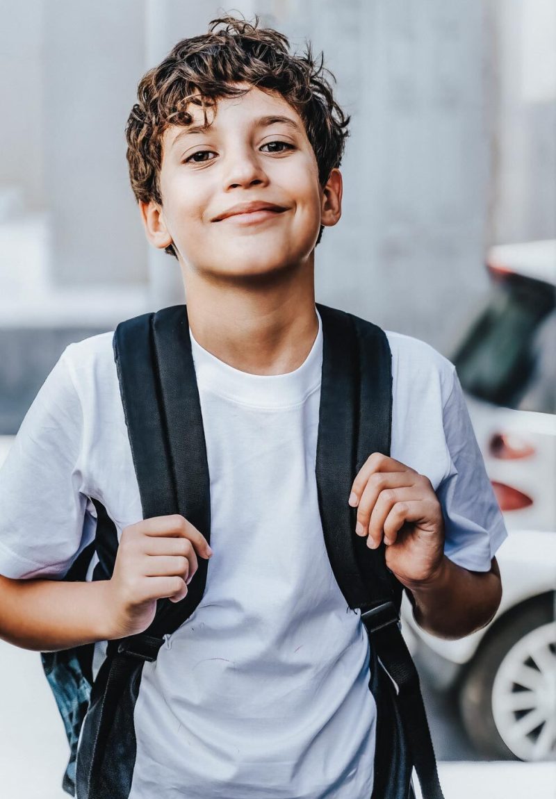 Cute handsome schoolboy with backpack going to school, urban street portrait - people lifestyle concept