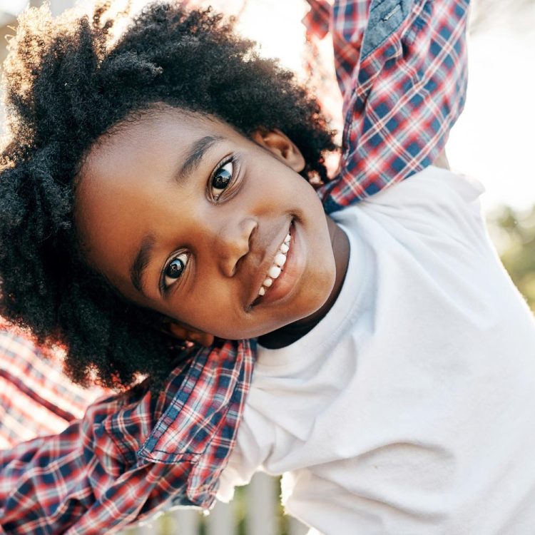 Portrait of a cheerful little boy playing around while looking into the camera outside during the day
