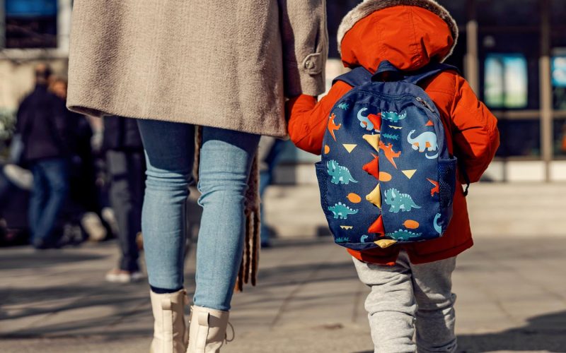 A mother entering the kindergarten yard with her preschooler boy.