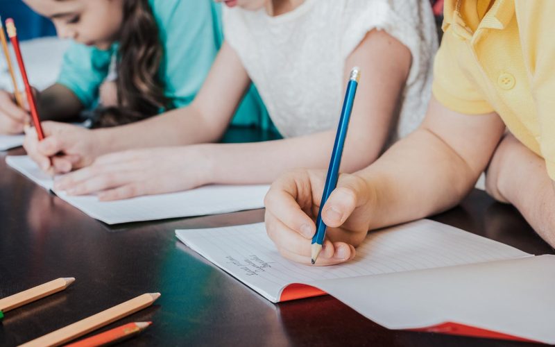 Close-up partial view of schoolchildren writing with pencils