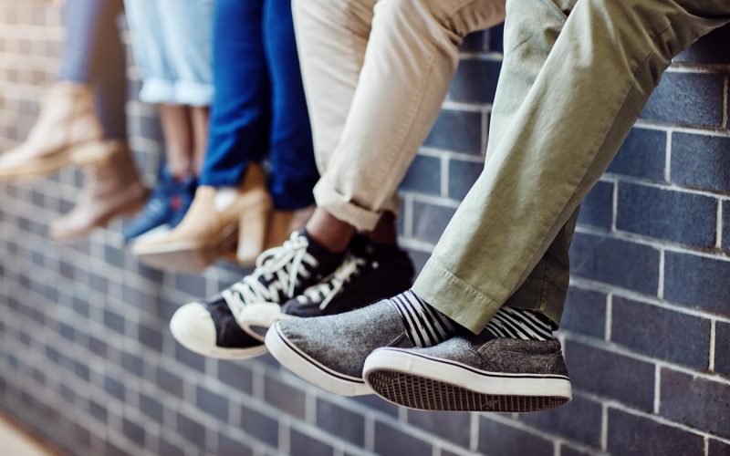 Closeup shot of an unidentifiable group of university students sitting together on a wall outside