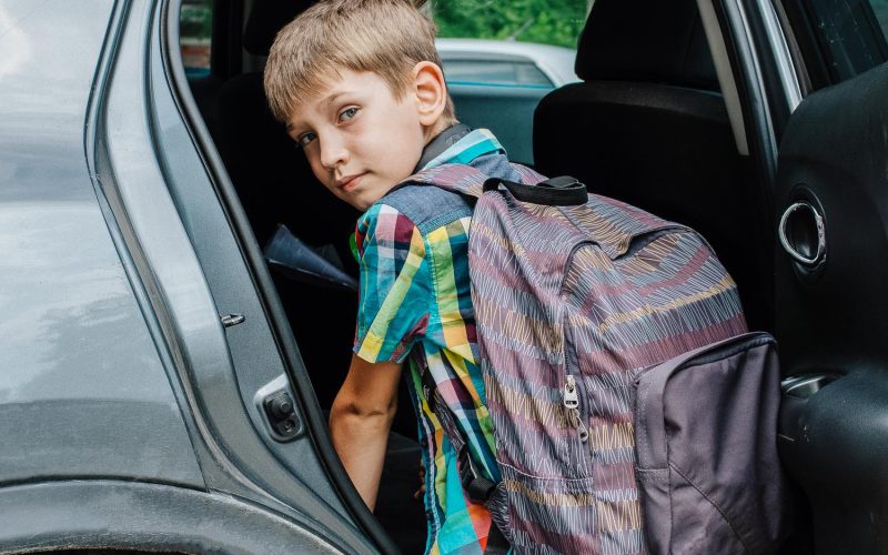 Portrait of smiling boy with school bag loosing into car. Taking a pupil after school. The boy gets into the car