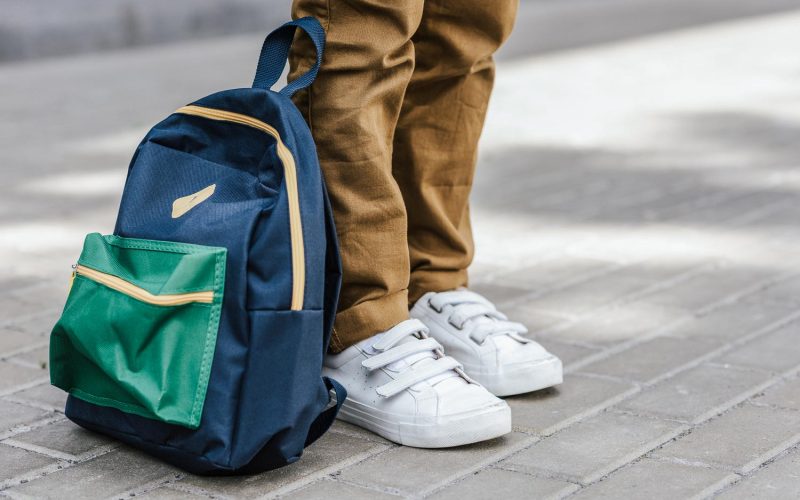 cropped shot of stylish schoolboy standing with backpack on street