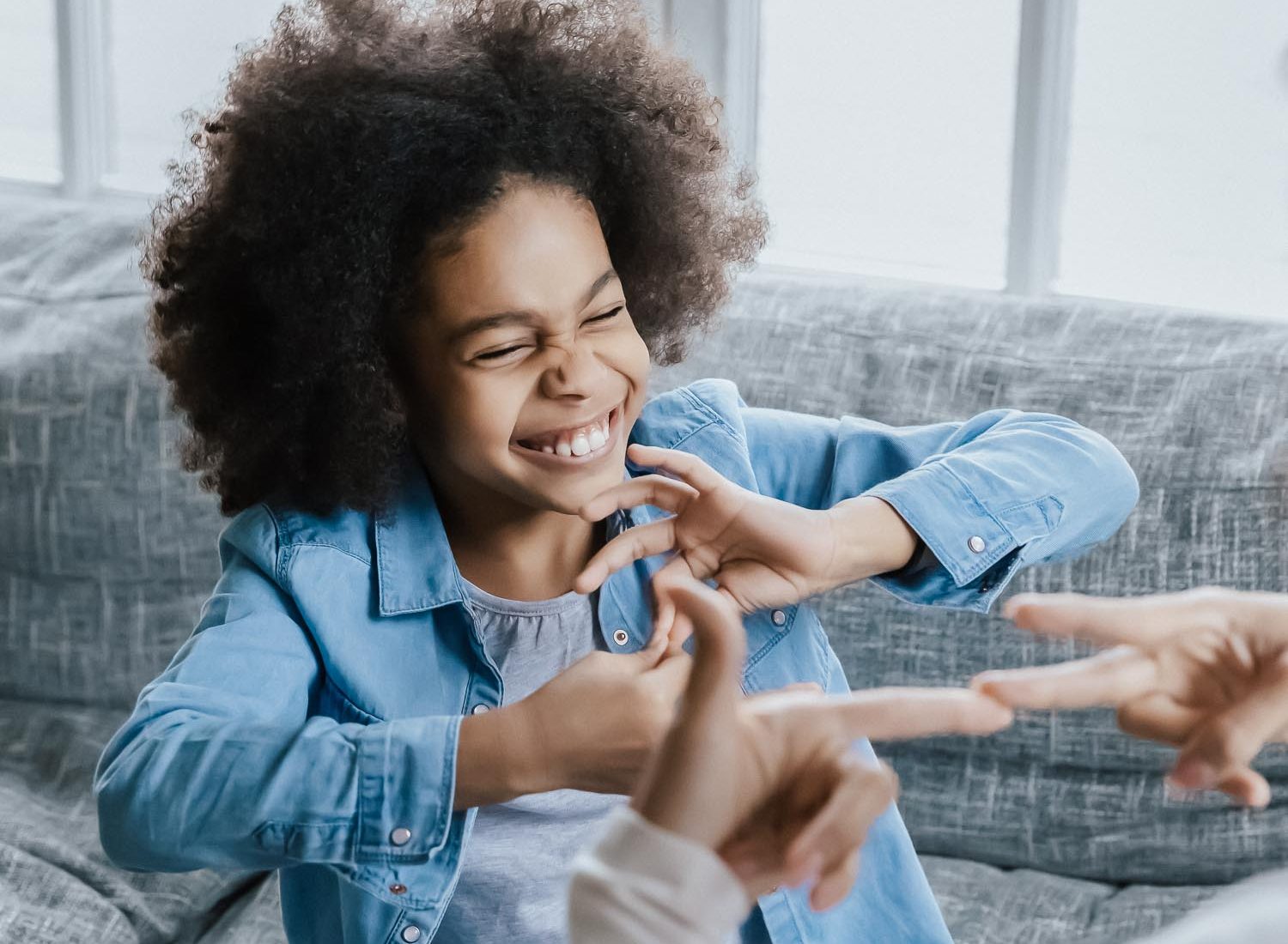 African deaf kid girl and her mother sitting on couch showing symbols with hands using visual-manual gestures enjoy communication at home. Hearing loss disability sign language learning school concept