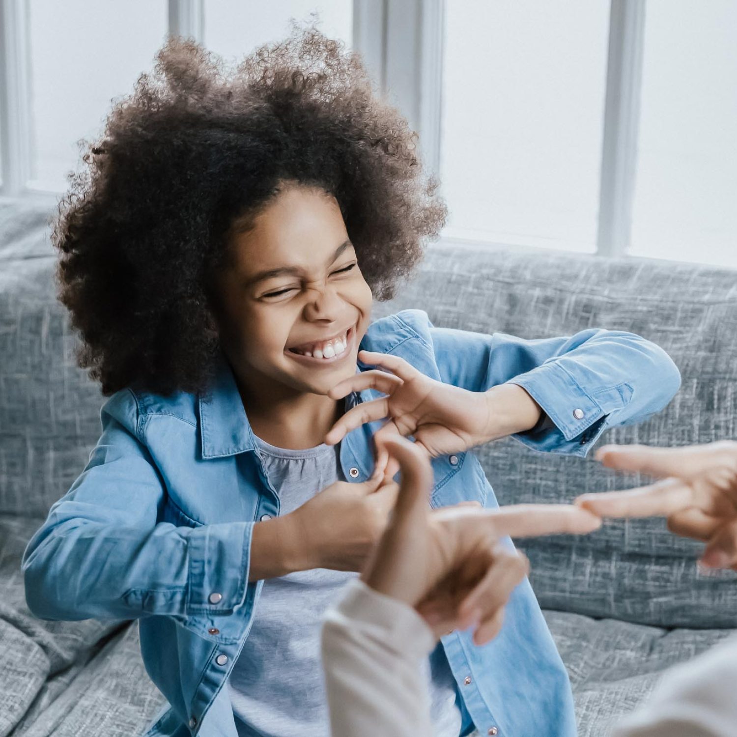 African deaf kid girl and her mother sitting on couch showing symbols with hands using visual-manual gestures enjoy communication at home. Hearing loss disability sign language learning school concept