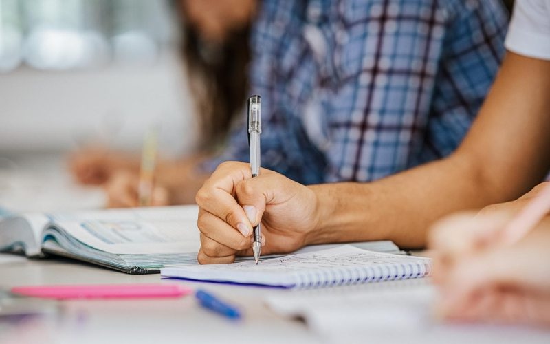 Close up of african student hand on table in classroom taking notes. Closeup of guy hand studying for exam in high school library. University student taking notes in classroom during lecture.