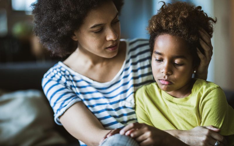 Young black mother taking care of her depressed little daughter at home.