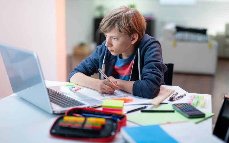 Boy having video conferences with a tutor on the computer at home. The concept of distance learning. The boy watches the lesson online and does homework remotely via the Internet.