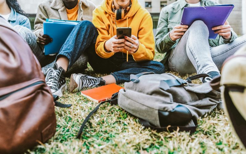 International students sitting together on green campus lawn - Group of high school teens studying outside college - Multiethnic millenial friends doing homework in university park - Academic concept