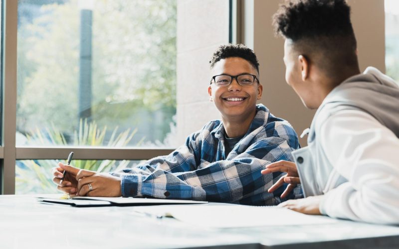 Waiting for class to start, the teenage boy smiles as he listens to his teen friend tell a story.