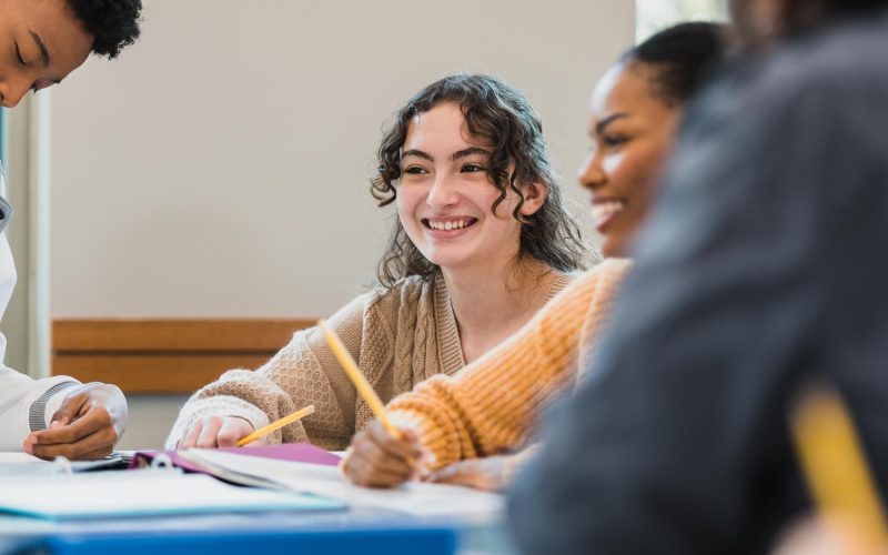 Multi-ethnic teens smile as they interact in the classroom.