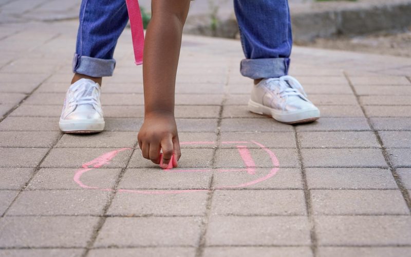 girl drawing with chalk on the school playground floor. Back to school concept. Multiethnic children group