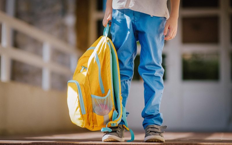 Little student with a backpack on the steps of the stairs of school building. Close-up of child legs, hands and schoolbag of boy standing on staircase of schoolhouse. Kids back to school concept.