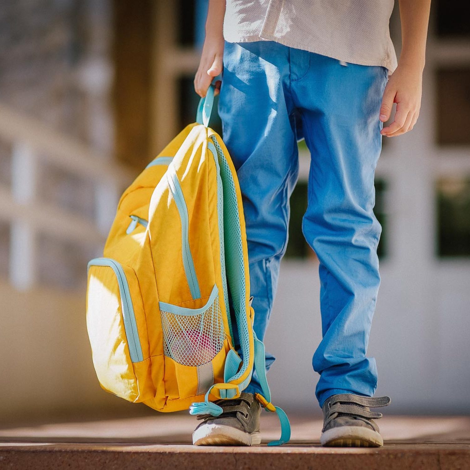 Little student with a backpack on the steps of the stairs of school building. Close-up of child legs, hands and schoolbag of boy standing on staircase of schoolhouse. Kids back to school concept.