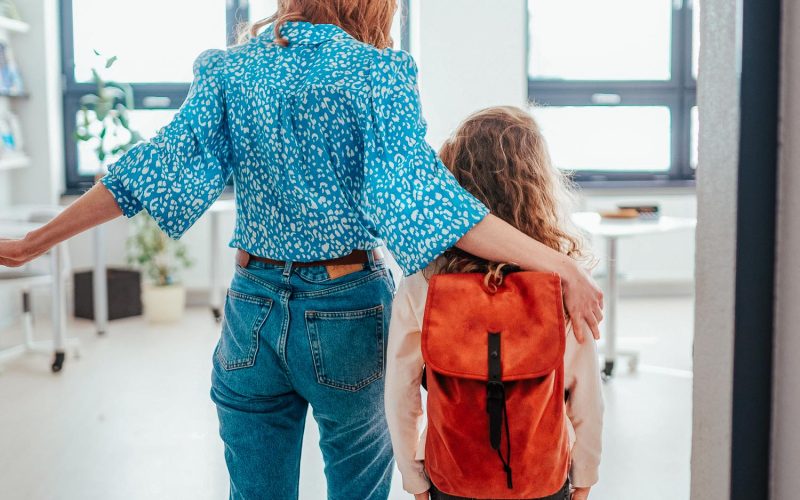 Rear view of teacher with Ukrainian schoolgirl in classroom, concept of enrolling Ukrainian kids to schools.