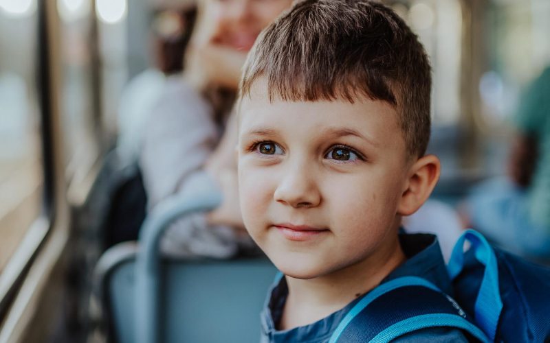 Close-up of little boy travelling to school by bus in the morning, commuting and sustainable lifestyle concept.