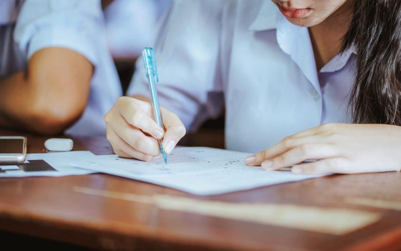 Student hand holding pen writing doing examination in university ,girl in uniform attending exam classroom educational school: college people in room ,Scholarship test for Study abroad