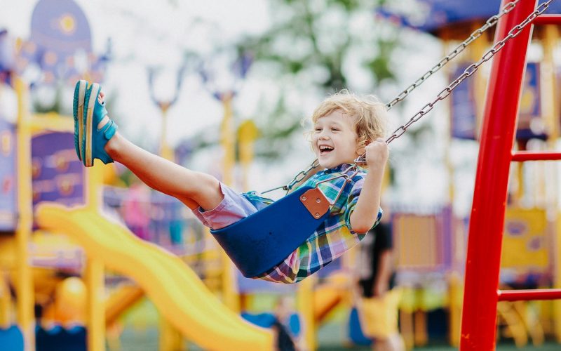 Child on swing playing on outdoor playground. Kids play on school or kindergarten yard. Active kid swinging. Healthy summer activity for children. Little boy having fun outdoors.