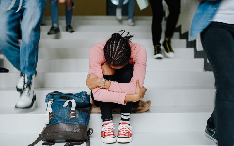 Depressed young student with face mask sitting on floor back at college or university, coronavirus concept.