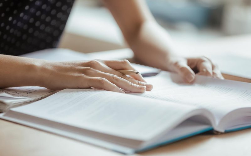 Student preparing for college test, exam, reading book, studying textbook, writing notes, making summary for class report. Learning workplace table, hands with pencil close up