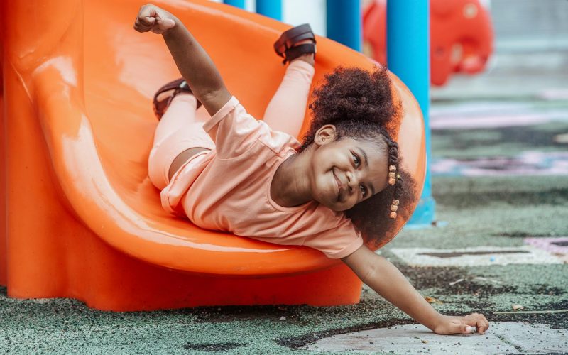 Happy African child girl sliding and playing at outdoor playground in the park on summer vacation, outdoor activity at school or or playground