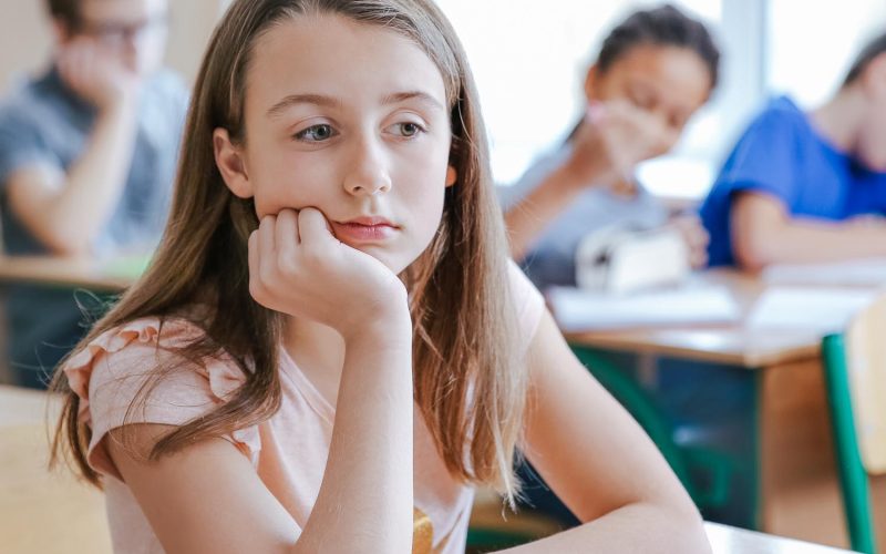 Sad girl sitting in classroom. Bullying at school