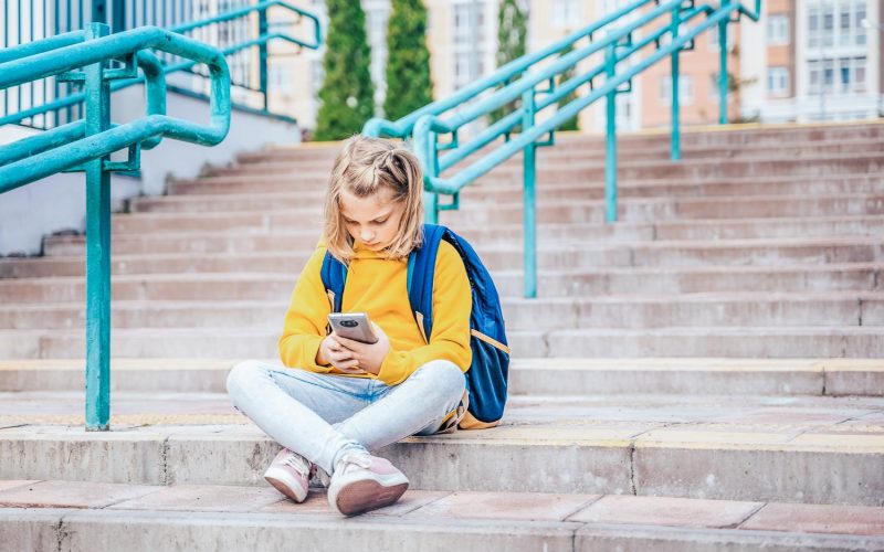 Back to elementary, primary school. Little girl with backpack,mobile phone. Chat, talk with friends, classmates on break. Autumn study after vacation. Education of children. Pupil kid on stair steps.