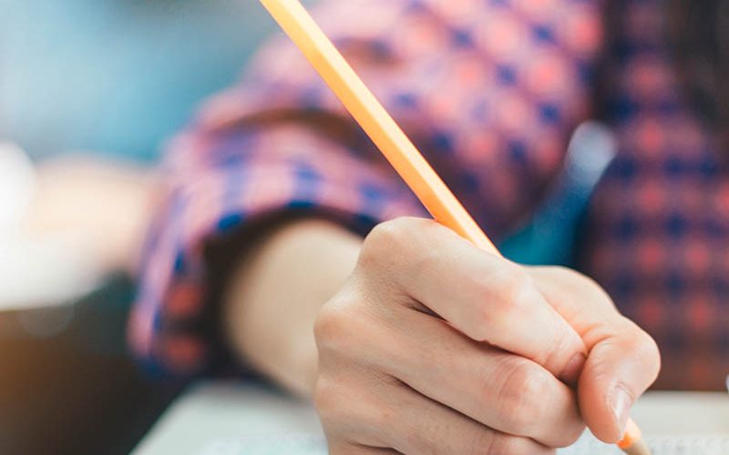 high school or university student holding pencil writing on paper answer sheet.sitting on lecture chair taking final exam attending in examination room or classroom.student in uniform