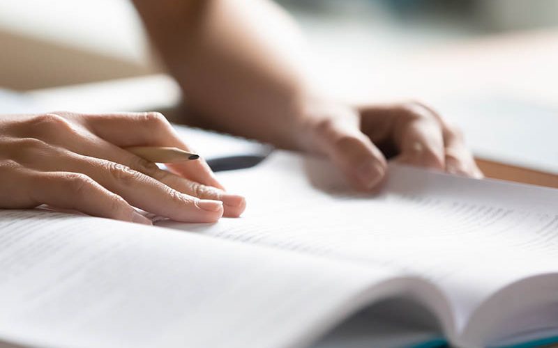 Student preparing for college test, exam, reading book, studying textbook, writing notes, making summary for class report. Learning workplace table, hands with pencil close up