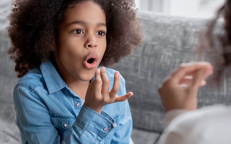 Close up disabled African American girl practicing sign language with mother or teacher, showing symbols, using gestures, interacting, repeating sounds, involved in speaking lesson at home