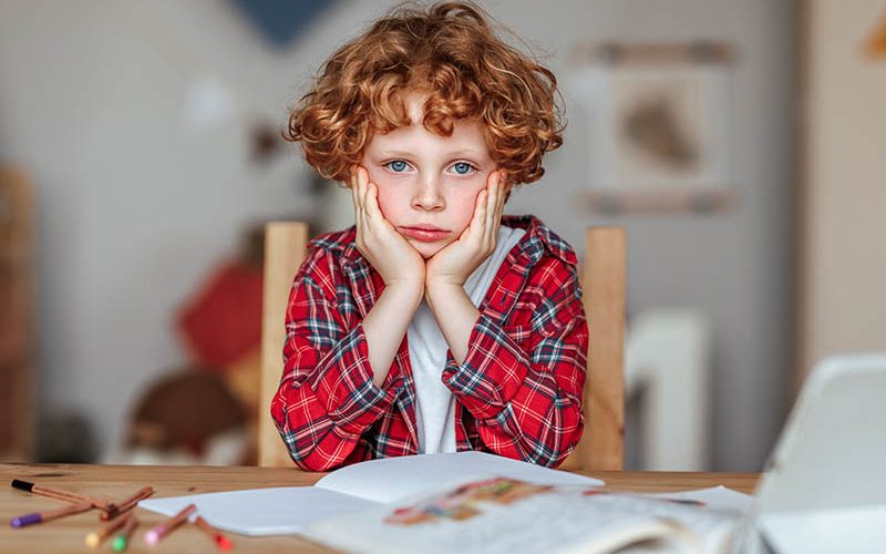 Frustrated boy thinking over difficult task and touching head while doing homework at table