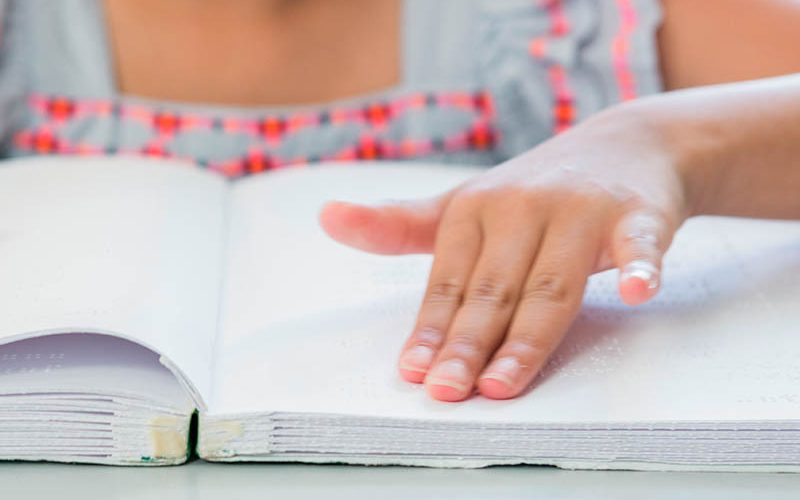Midsection of blind girl reading braille book in classroom